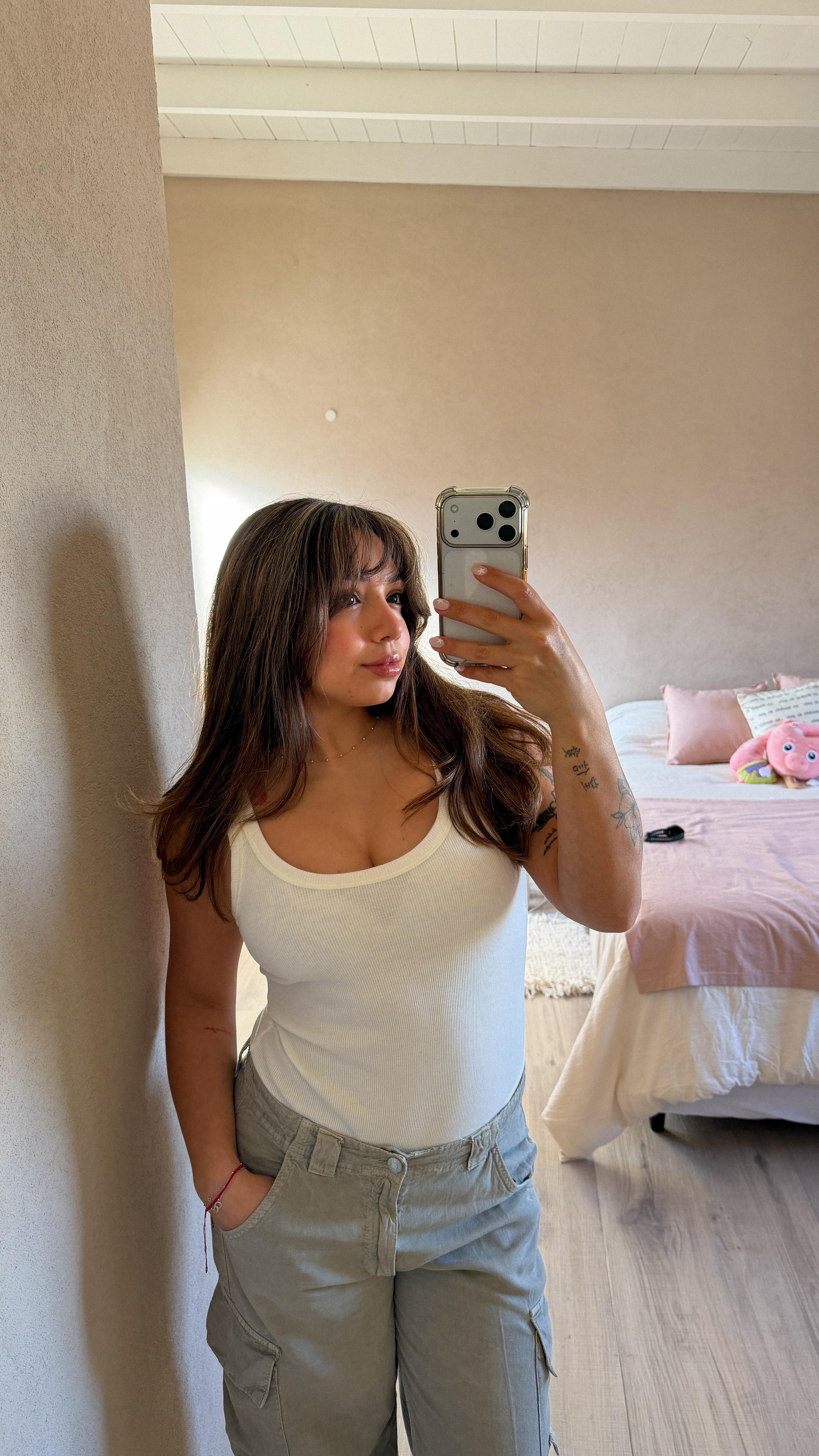Sofia taking a mirror selfie in a white tank top and sage cargo pants in a cozy pink bedroom
